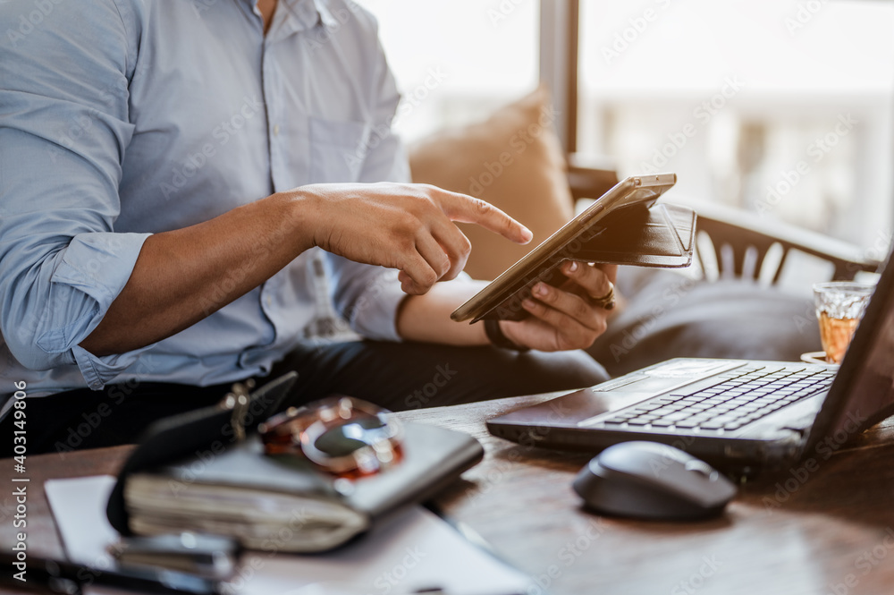Fototapeta premium Businessman using tablet with laptop and pen on wooden table in coffee shop..Business and working concept