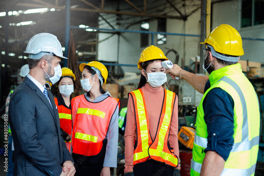Foreman hold digital thermometer, measure temperature for screen workers with face mask, prevent against infection of Covid-19 outbreak, industrial engineers in line at manufacturing industry factory Foreman hold digital thermometer, measure temperature for screen workers with face mask, prevent against infection of Covid-19 outbreak, industrial engineers in line at manufacturing industry factory