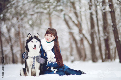 Girl sitting in the snow with a siberian husky dog in the winter forest