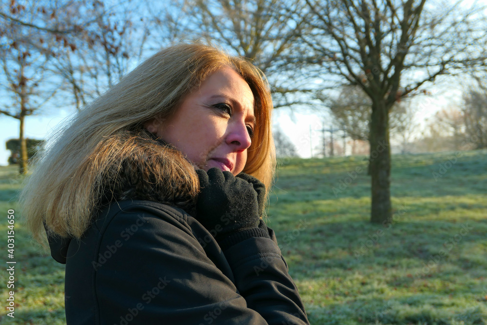 Portrait of a lovely blonde woman with long hair, aged between forty and fifty years. People outdoor in a park in winter. Background blurred voluntarily.