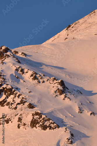 An industrious snowboarder climbs a steep, rugged mountain in Alaska's Talkeetna Range for a sunny winter morning ride. photo