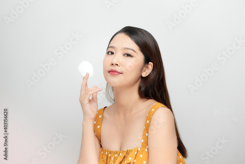 Photo of a beautiful young pretty asian woman with healthy skin posing naked isolated over white wall background holding cotton pads.