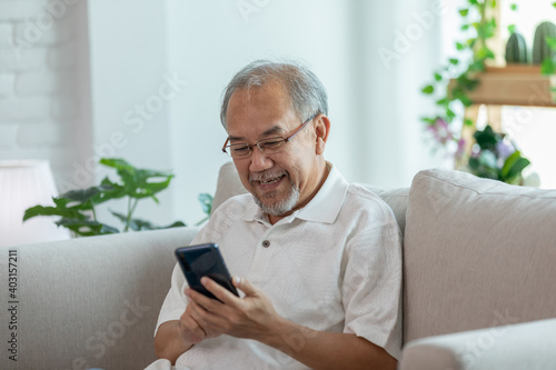 Happiness elderly asian man sitting on sofa using mobile phone and social media smile at home,Senior lifestyle at home concept