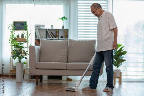 Asian Elderly senior man cleaning dust in living room by Wireless Vacuum cleaner
