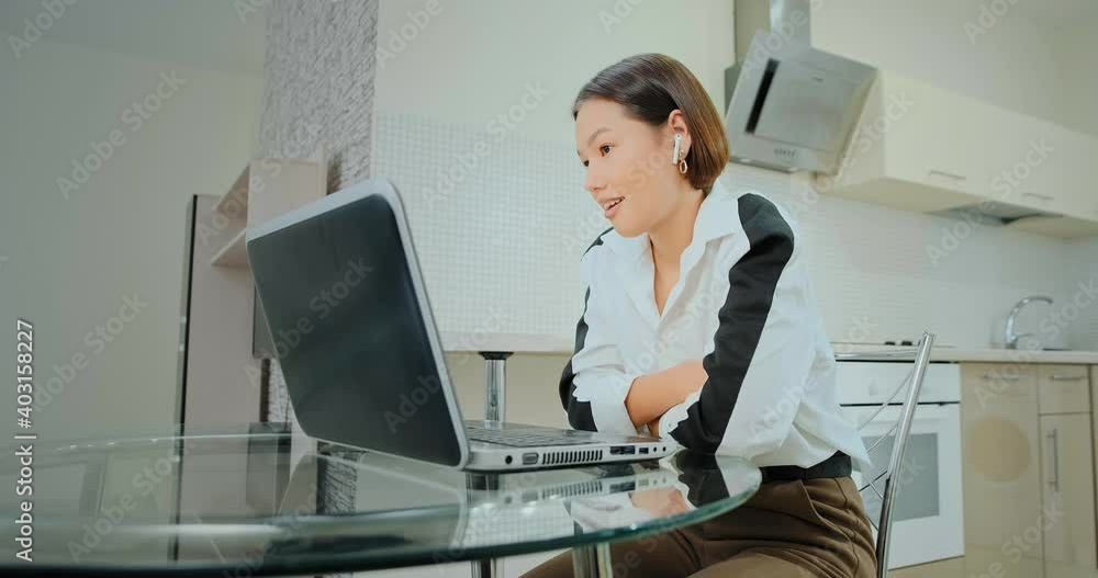 Professional manager with white headphones looks at black laptop display and talks to colleagues during online conference at home Professional manager with white headphones looks at black laptop display and talks to colleagues during online conference at home