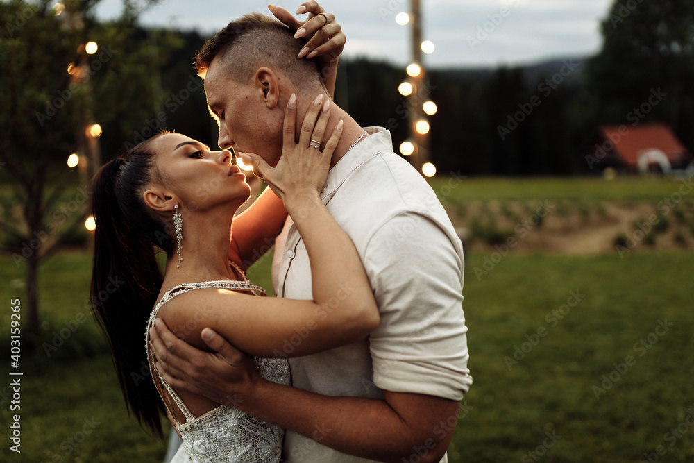 Fototapeta premium Portrait of beautiful elegant couple kissing. Handsome man hugging attractive woman, enjoy tenderness. Gorgeous lady with attractive male walking at the park, spend weekends outdoor together
