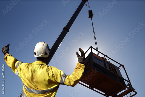Rigger wearing a glove standing raising using his hands signal by moving finger slowly to directing communication with crane driver to move the boom up at construction site, Sydney, Australia   
