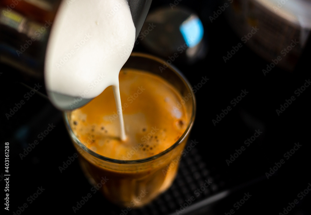 Close focus on pouring steam milk into shot of hot espresso coffee on glass cup. Close focus on pouring steam milk into shot of hot espresso coffee on glass cup.