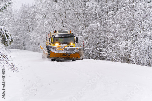 A snow blower car clears snow in the forest from the road on a winter morning. Snow plow truck cleaning icy white road