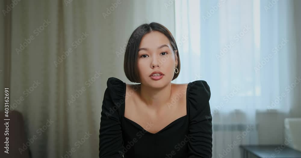 Concentrated freelancer in black blouse talks to employer via video call sitting at home against white window curtains closeup Concentrated freelancer in black blouse talks to employer via video call sitting at home against white window curtains closeup