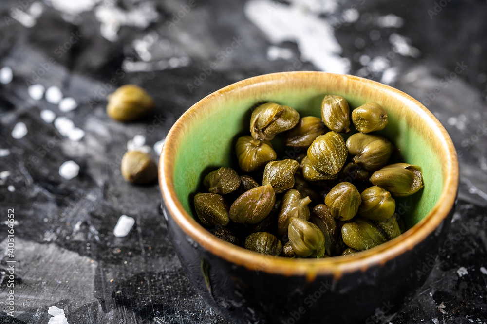Marinated capers in a ceramic bowl. Edible flower buds of Capparis spinosa, caper bush or Flinders rose on a dark background Marinated capers in a ceramic bowl. Edible flower buds of Capparis spinosa, caper bush or Flinders rose on a dark background