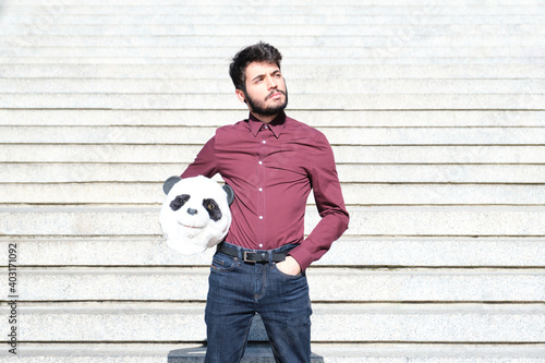 Young business man with a panda head mask in his hands, standing on stairs. Bizarre businessman.