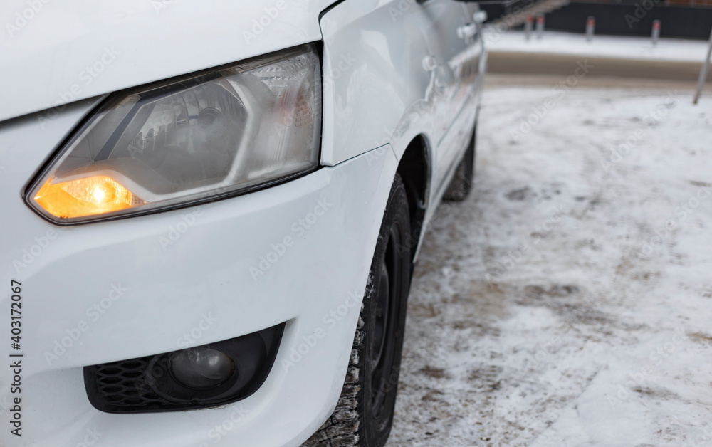 A white car stands in a city parking lot in winter close-up. blurred focus
