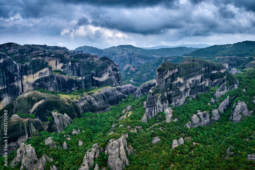 View over impressive pillars of sedimentary rocks in iconic Meteora valley at cloudy spring day. Hills covered with trees, winding roads, Greece