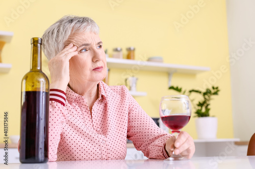 Stressed senior woman drinking wine at home