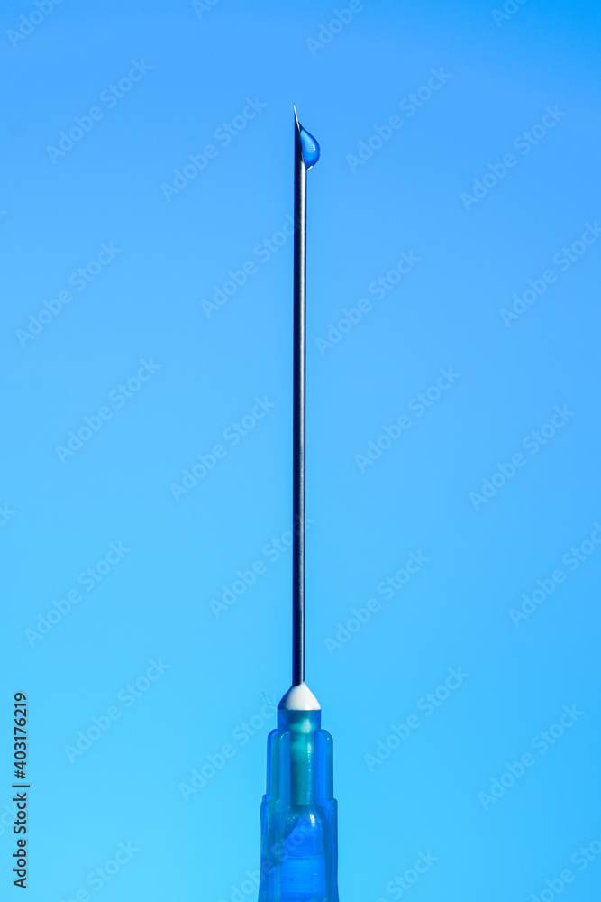 Syringe needle with liquid drop on the tip macro close up isolated on blue Syringe needle with liquid drop on the tip macro close up isolated on blue