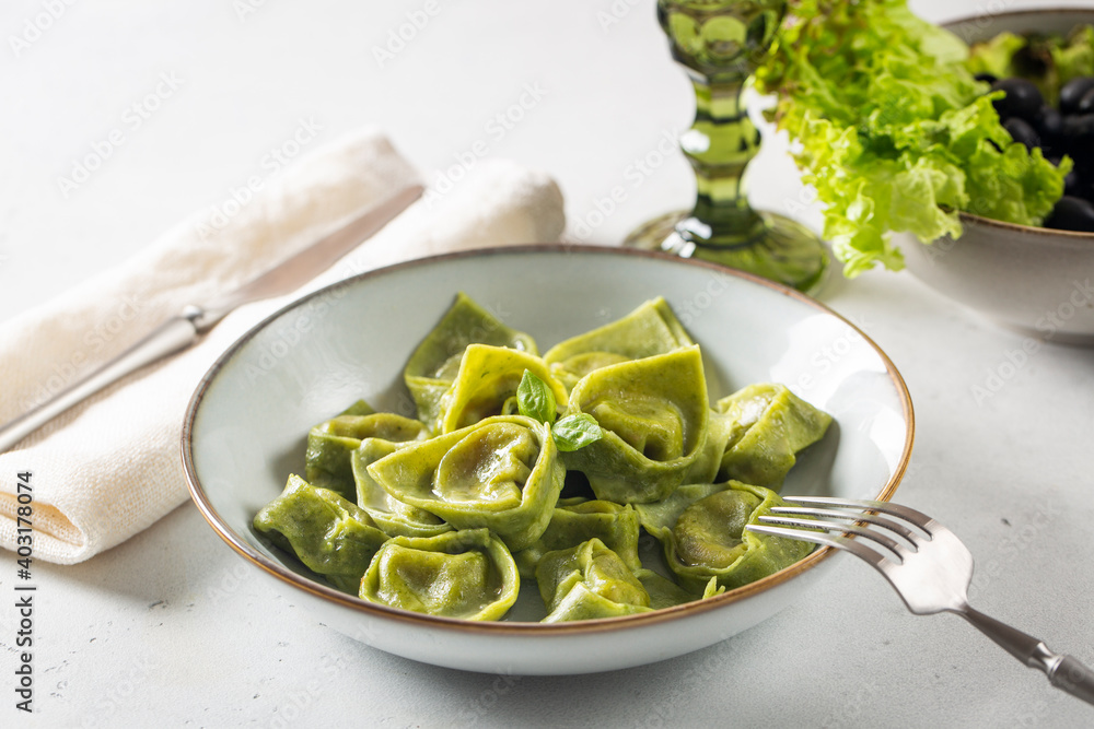 Homemade tortelli - italian green pasta, dough made with eggs and spinach,  filled with ricotta and spinach. Light background.