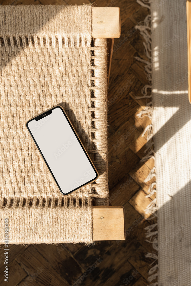 Blank screen smart phone on rattan chair. Flat lay, top view. Copy space mockup template. Warm sunlight shadows. - obrazy, fototapety, plakaty 