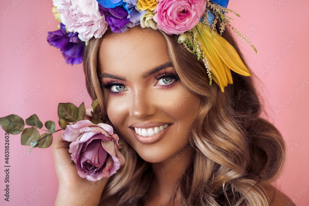 Beautiful young woman with flowers in her hair posing on pink backgroud