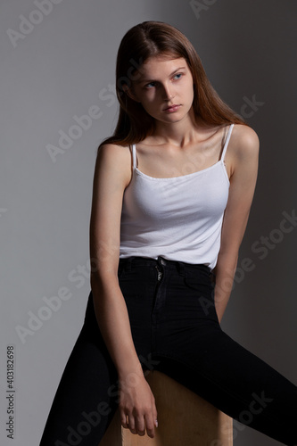 beautiful girl in a white t-shirt and black sweatpants posing while sitting on wooden cubes in the studio on a gray background