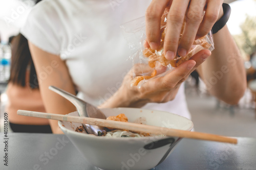 Woman in white t-shirt eats pork rind or pork crackling with Thai noodle.