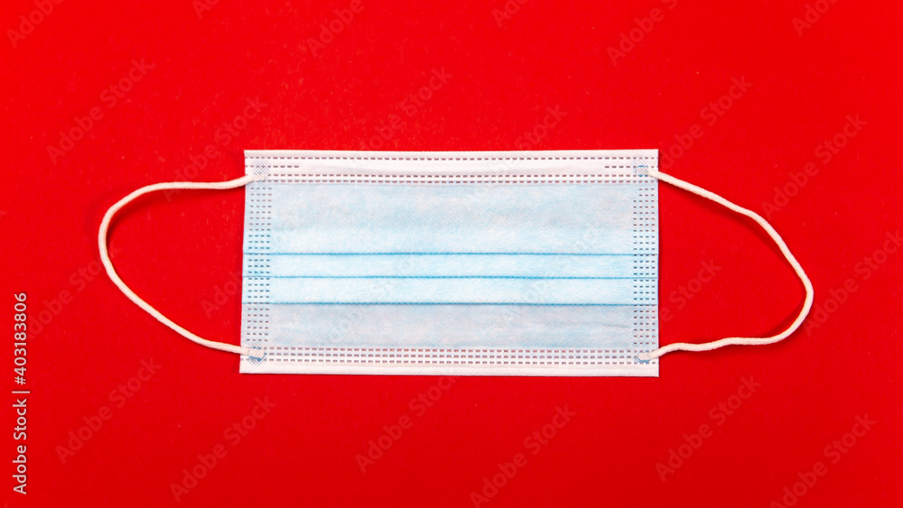 Close up shot of blue face travel surgical hygienic disposable mask isolated red background. Healthcare medicine. Protection prevent infection, illness against coronavirus seasonal disease flu. Close up shot of blue face travel surgical hygienic disposable mask isolated red background. Healthcare medicine. Protection prevent infection, illness against coronavirus seasonal disease flu.