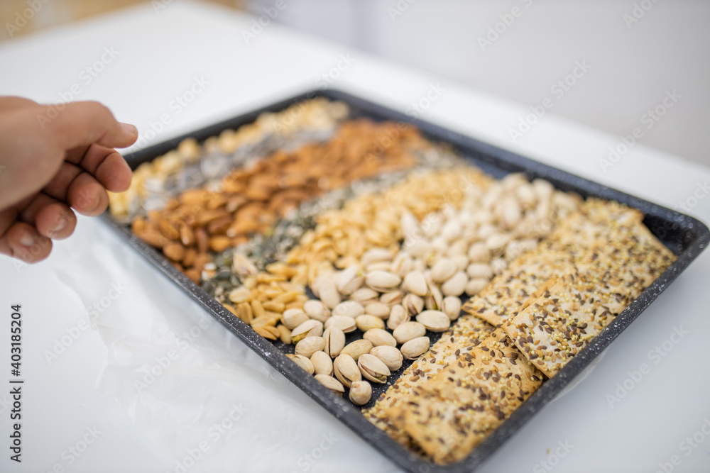Black tray of nuts and seeds above a white table Black tray of nuts and seeds above a white table