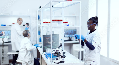 Multiethnic scientists team working together in modern facility doing virus analysis. Black healthcare researcher in biochemistry laboratory wearing sterile equipment.