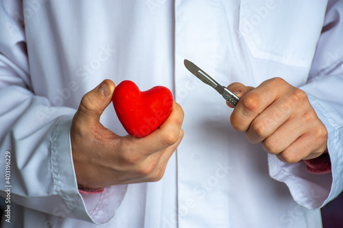 Heart surgery or cardiac surgery (cardiosurgery). Doctor surgeon holding scalpel in hand and cut red heart shape on white background. Concept for surgical operations on heart in adults and children photo