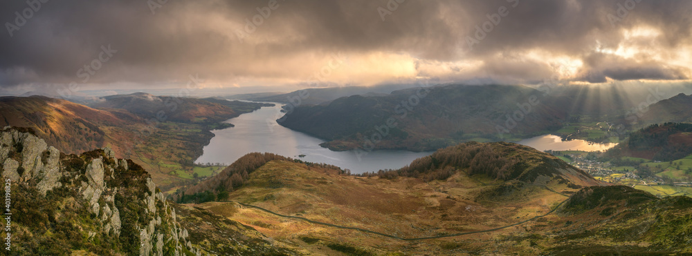 Panorama of dramatic clouds with a view over Ullswater in the Lake District as shafts of sunlight casts rays over Glenridding village