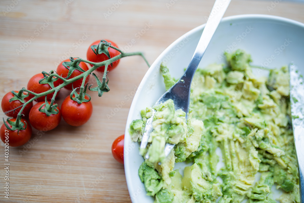 Cherry tomatoes and bowl of mashed avocado on wooden table Cherry tomatoes and bowl of mashed avocado on wooden table