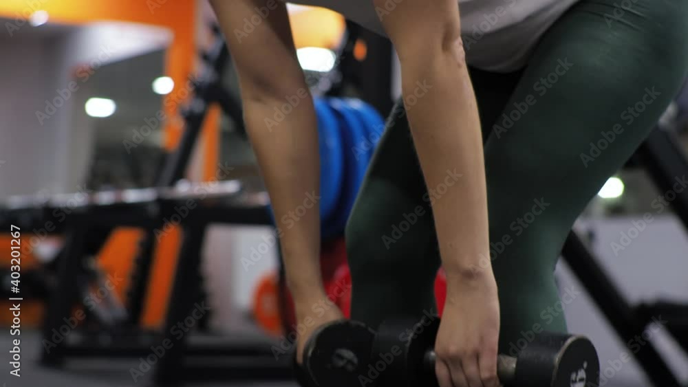 Gym. Lesson with a young funny trainer man. A beginner young woman shakes her back forward bends with dumbbells. Gym. Lesson with a young funny trainer man. A beginner young woman shakes her back forward bends with dumbbells.