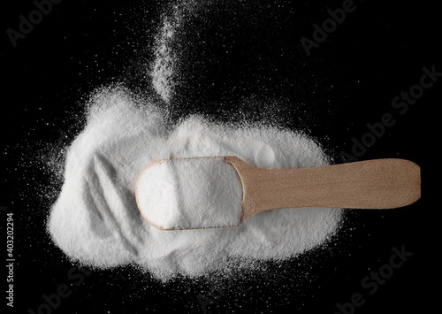 Valokuva Baking soda pile, sodium bicarbonate with wooden spoon isolated on black backgro