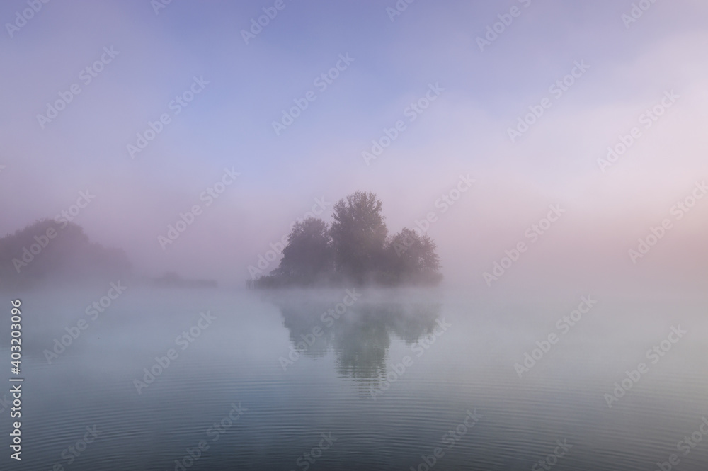 Fototapeta premium island in lake on foggy autumn morning, reflected in water.