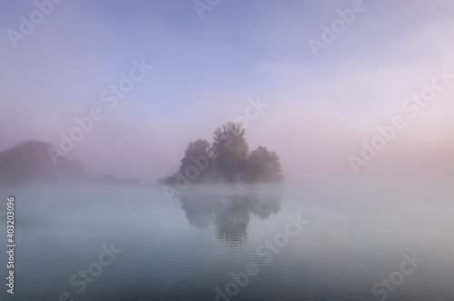 island in lake on foggy autumn morning, reflected in water.