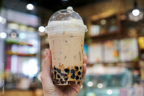 Woman holding a plastic cup of milk tea and brown sugar boba or bubble drinks. Center focus. Bokeh background.