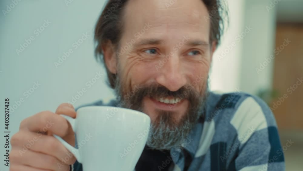 Confident and natural, authentic looking handsome middle aged man with grey beard enjoy drinking cup of coffee at home or at specialty coffee place. Bright blue eyes, chuckle and smile thinking Confident and natural, authentic looking handsome middle aged man with grey beard enjoy drinking cup of coffee at home or at specialty coffee place. Bright blue eyes, chuckle and smile thinking
