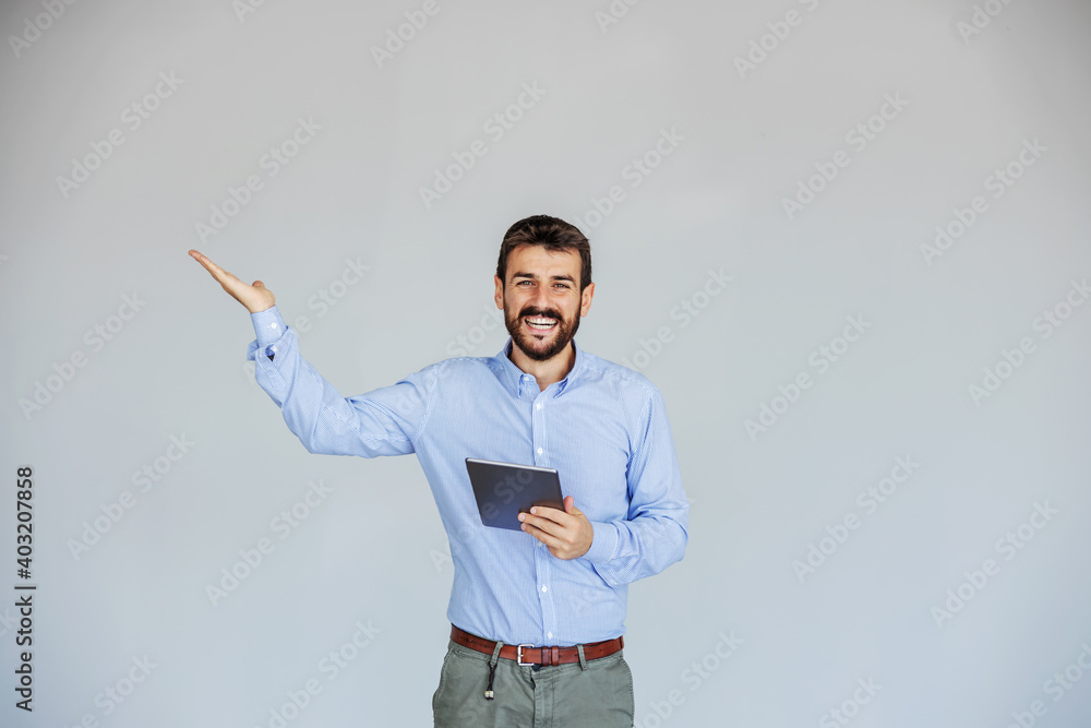 Smiling bearded businessman standing and holding tablet while looking at camera. He is gesturing like he is holding something. Smiling bearded businessman standing and holding tablet while looking at camera. He is gesturing like he is holding something.