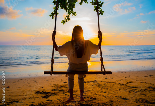 Woman sitting on a wooden swing by the sea during the beautiful sunset in holiday relax time