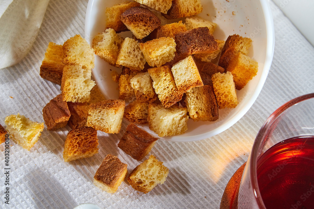 Square toasted pieces of homemade delicious rusk, hardtack, Dryasdust, zwieback on a plate and black tee in a cap on a white tablecloth. Square toasted pieces of homemade delicious rusk, hardtack, Dryasdust, zwieback on a plate and black tee in a cap on a white tablecloth.