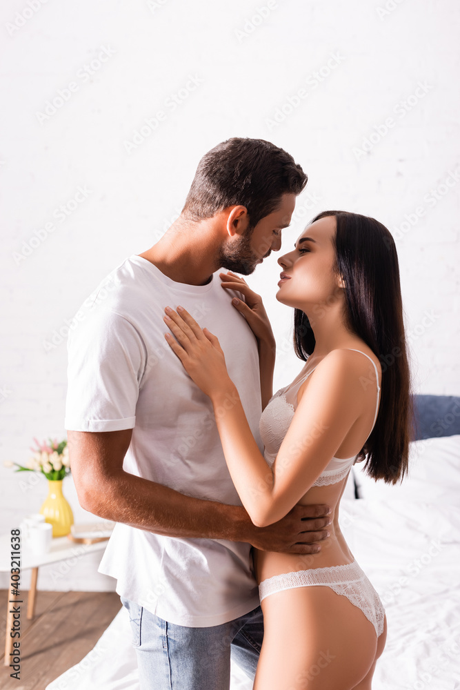 Naklejka premium sexy young couple hugging and looking at each other in bedroom