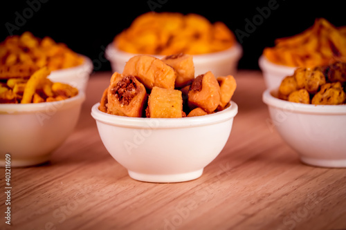 Indian morning or tea-time snacks like bhakharvadi , chivda, farsan, mixture, shing bhujia, bakarwadi etc served in white wooden box photo