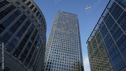 Ground level view of passenger airplane flying at high altitude above London city skyline, financial district, United Kingdom