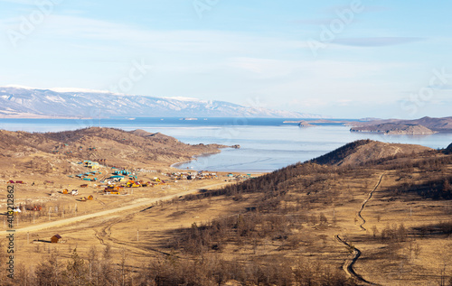 Baikal Lake in December. Freezing up in the Small Sea Strait. Top view of a dirt road to a popular resting place on the shores of the Kurkut Bay and tourist wooden houses on a winter day