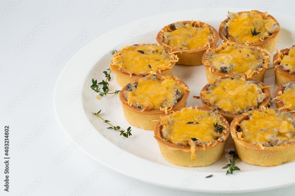 On a white plate, tartlets with mushroom filling and cheese. On a white plate, tartlets with mushroom filling and cheese.