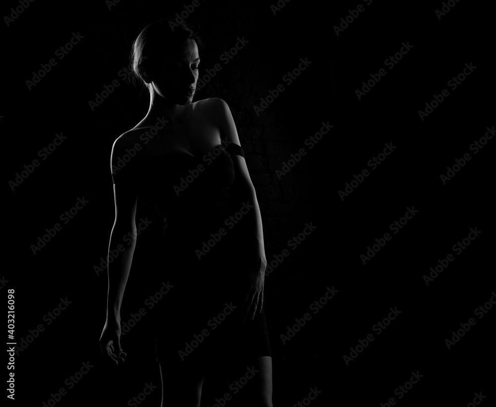 Black and white dark silhouette of a beautiful woman body on a dark background.