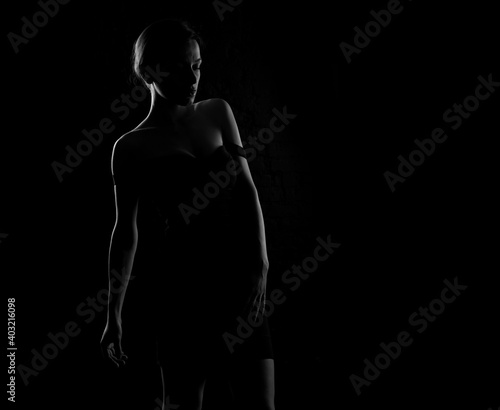 Black and white dark silhouette of a beautiful woman body on a dark background.