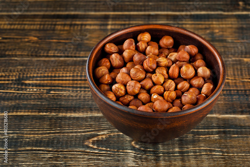 Hazelnuts in a clay bowl on an old shabby board. Nuts on a brown wooden table.