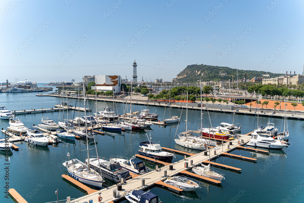 Many white yachts are moored in the port of Barcelona on a sunny summer day