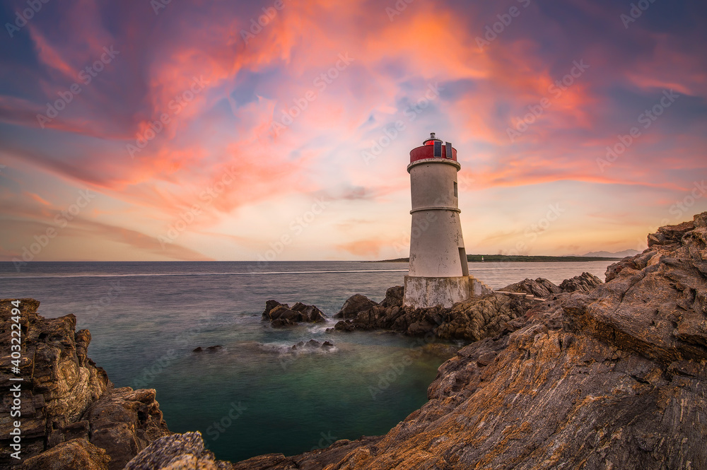 (Selective focus) Stunning view of a rocky coastline with a lighthouse during a dramatic sunset. Sardinia, Italy